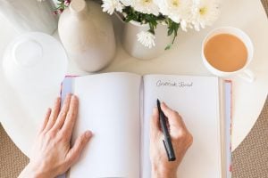 woman writing in a journal on a white table