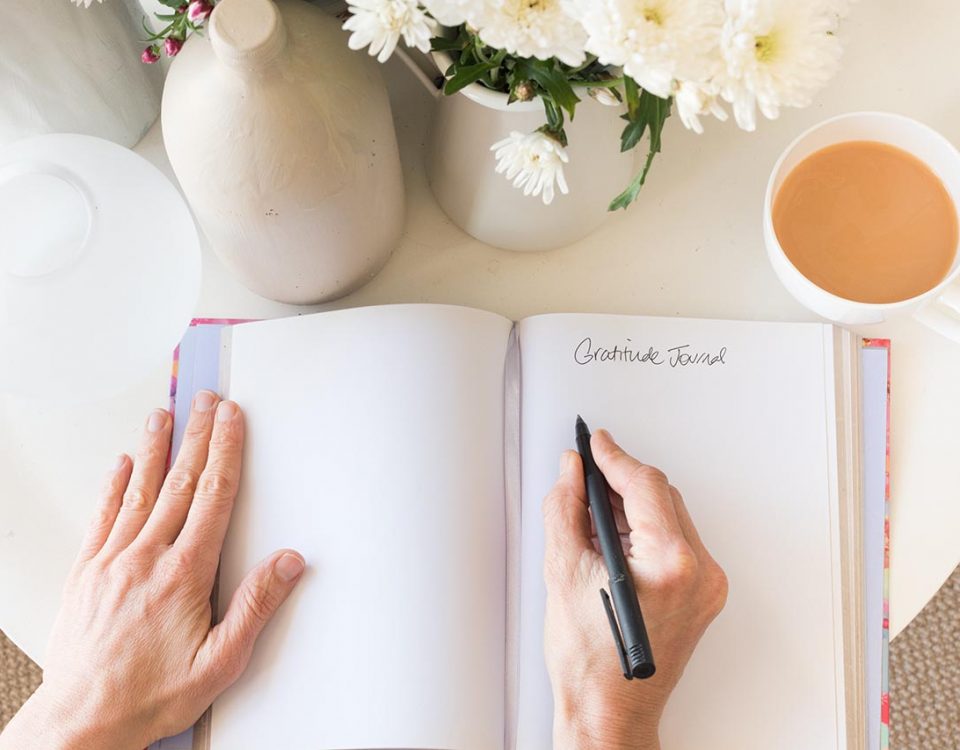 woman writing in a journal on a white table