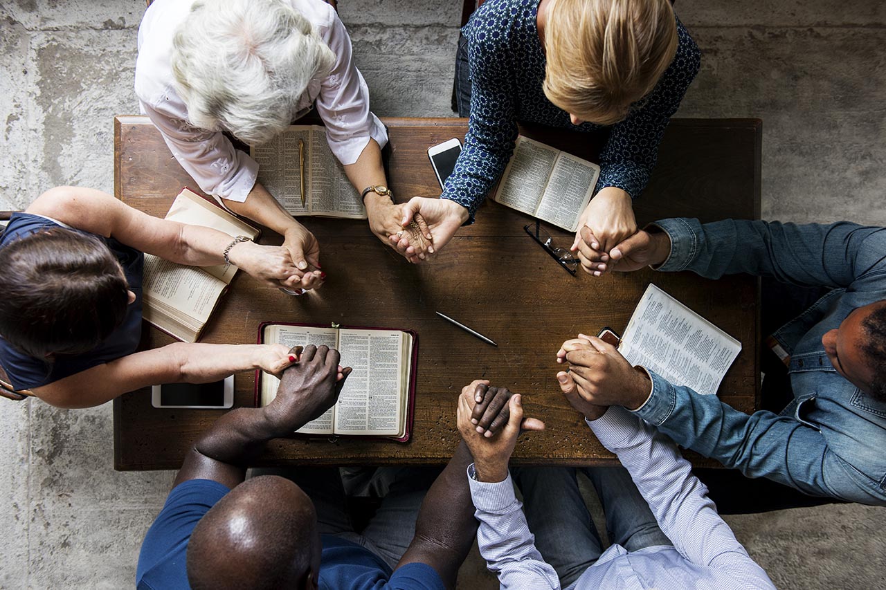 six people praying together at a wooden table