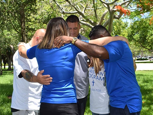 Group of Banyan staff and clients in a prayer circle outdoors during a Christian faith-based treatment program
